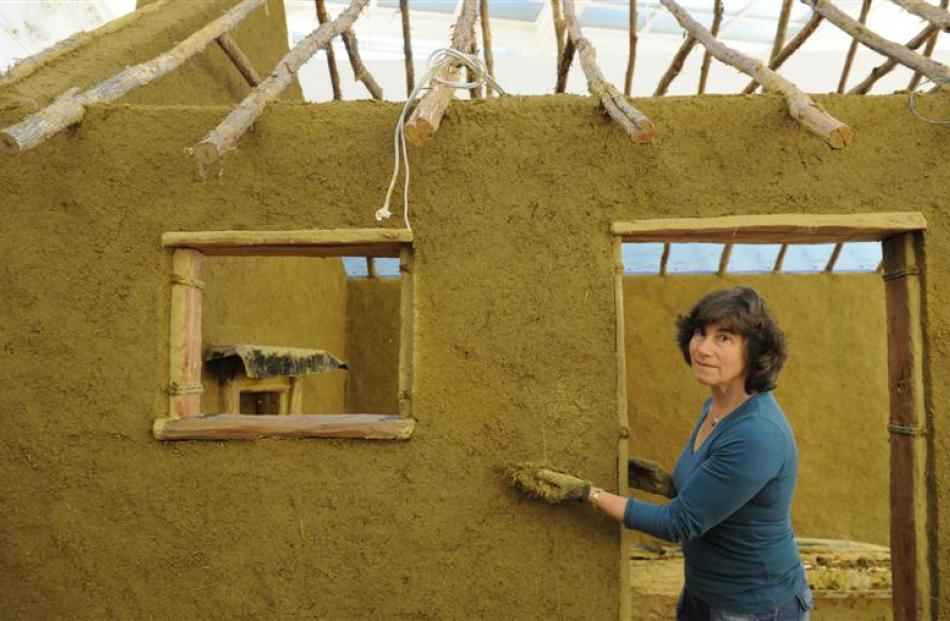 Helen Edwards, of Dunedin,   applies earthen plaster to a replica of a 19th century cottage being...