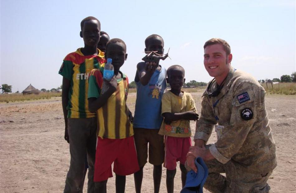 Major Cory Neale shares a bottle of water and a toy helicopter with children in South Sudan....