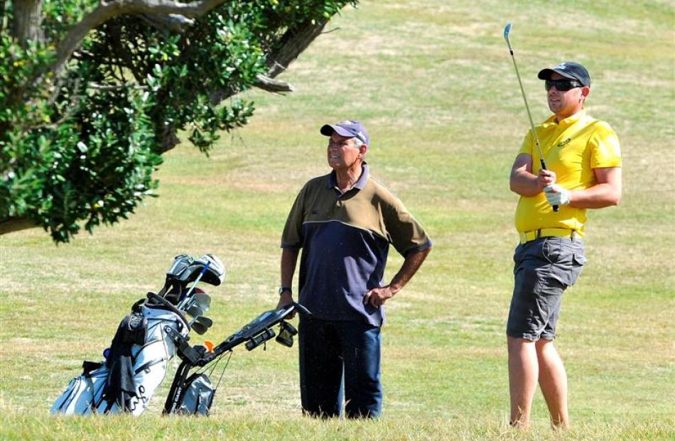 Michael Smith plays an iron from the 16th fairway, watched by his caddie, Alan Bartlett, during...