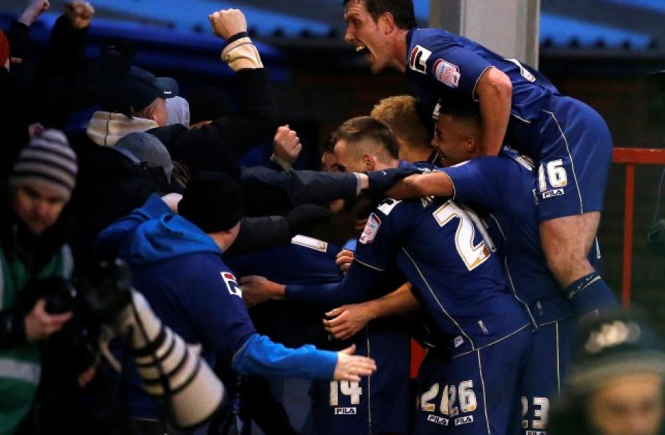 Oldham Athletic's Matt Smith (hidden) celebrates with teammates and supporters after scoring his...