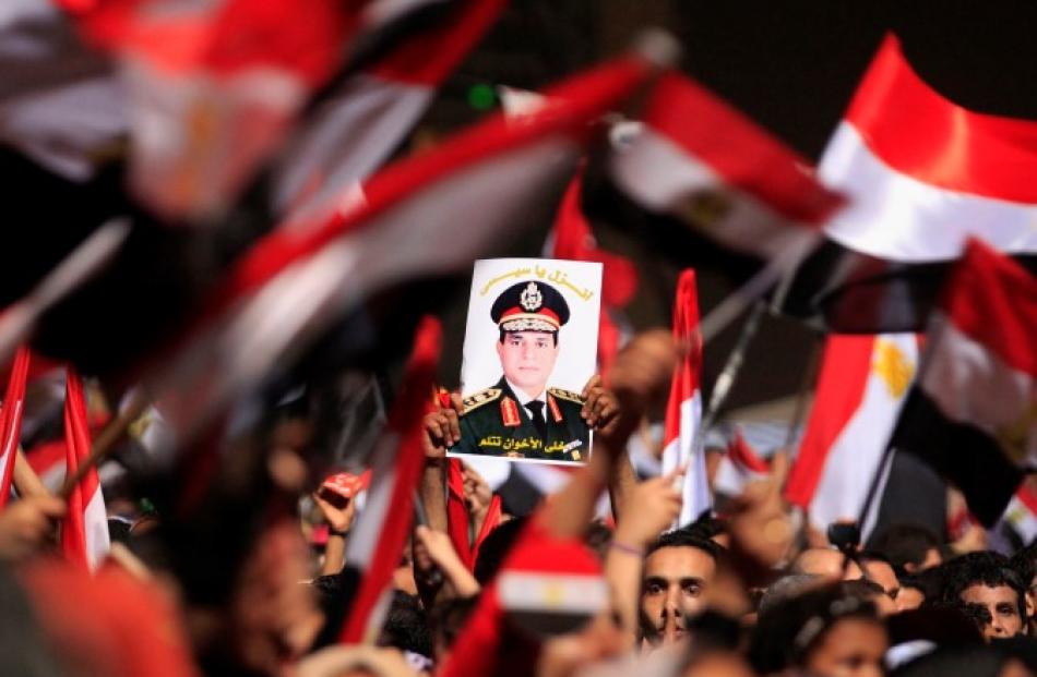 Opponents of Egyptian President Mohamed Mursi hold a poster featuring the head of Egypt's armed...