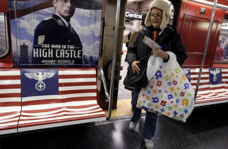 Passengers board a subway train, wrapped with advertising for the Amazon series "The Man in the...