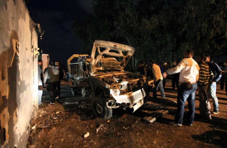 People stand near a police car that was destroyed in an explosion in front of a police station in...