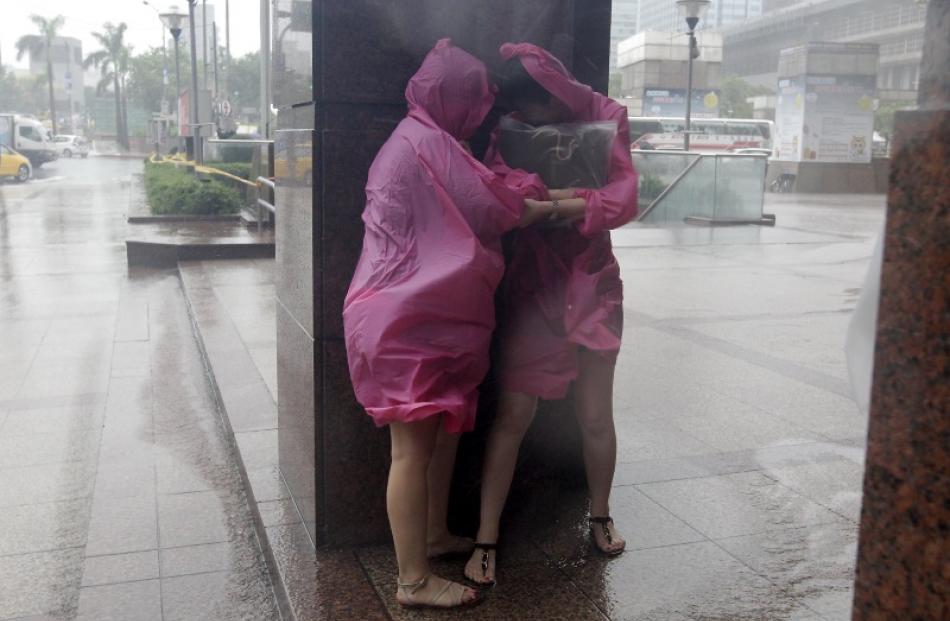People take shelter against strong winds caused by Typhoon Dujuan by standing behind the column...