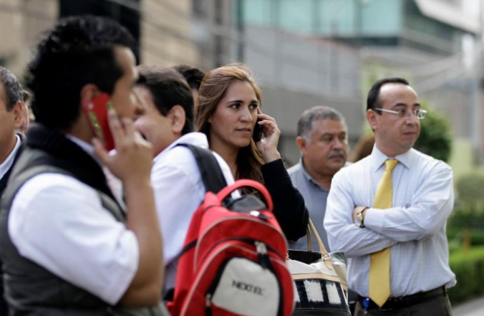 People talk on cellphones after being evacuated from their buildings following an earthquake in...