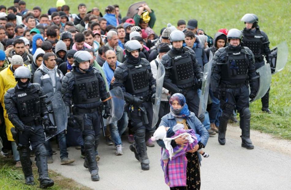 Police officers escort migrants as they make their way on foot after crossing the Croatian...