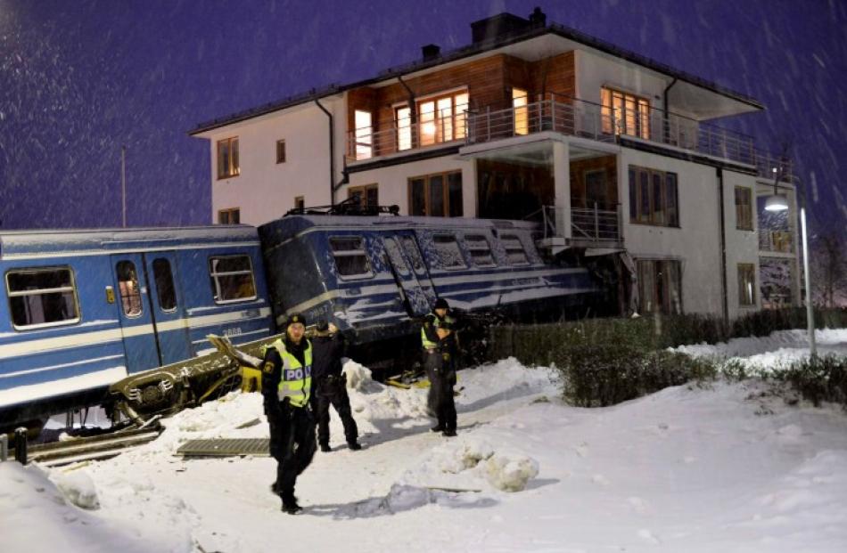 Police officers stand around a stolen train that derailed and crashed into a residential building...