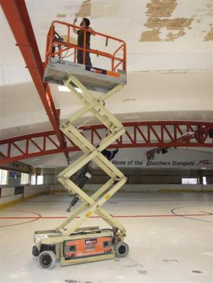 Queenstown Ice Arena co-owner Ted Graham paints the  rink's ceiling where condensation has...