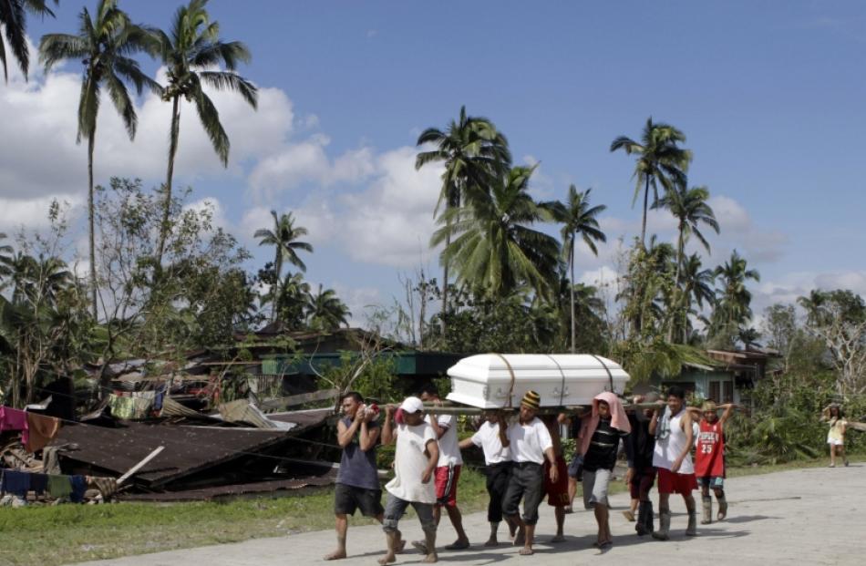 Residents carry the coffin of a typhoon victim past a destroyed house in New Bataan town in...