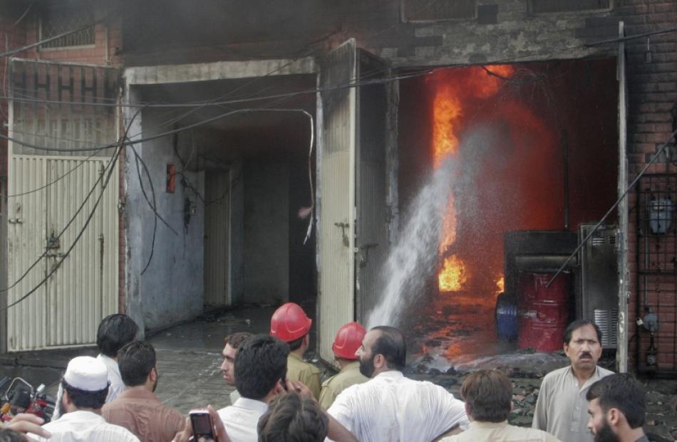 Residents gather while firefighters try to extinguish a fire at a shoe factory in Lahore. Photo...