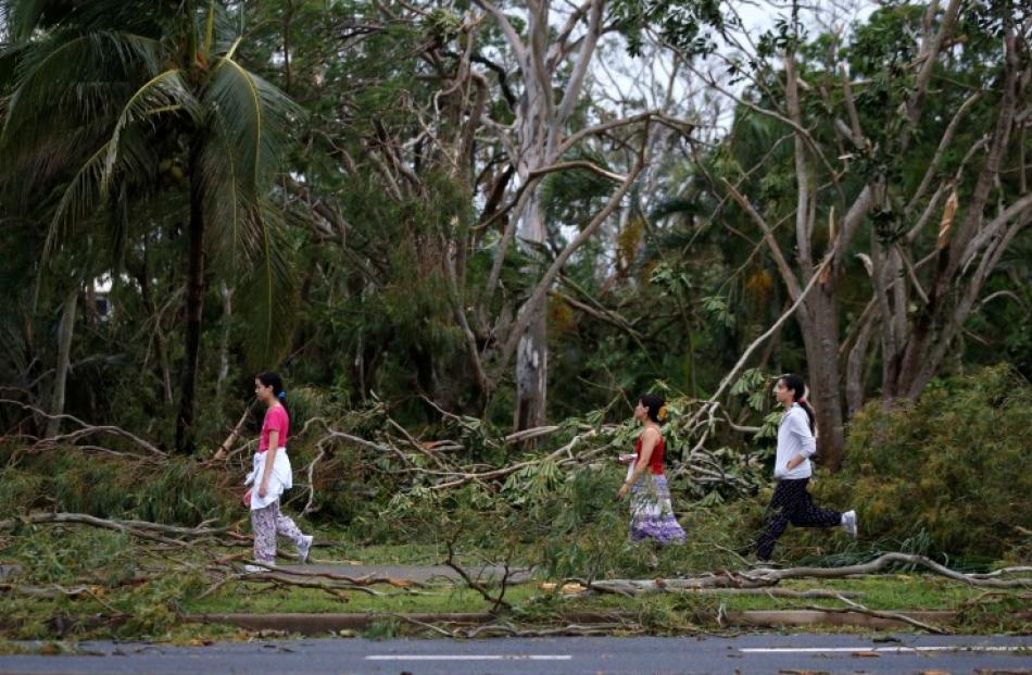 Residents of the coastal town of Yeppoon step through fallen trees alongside a damaged home after...