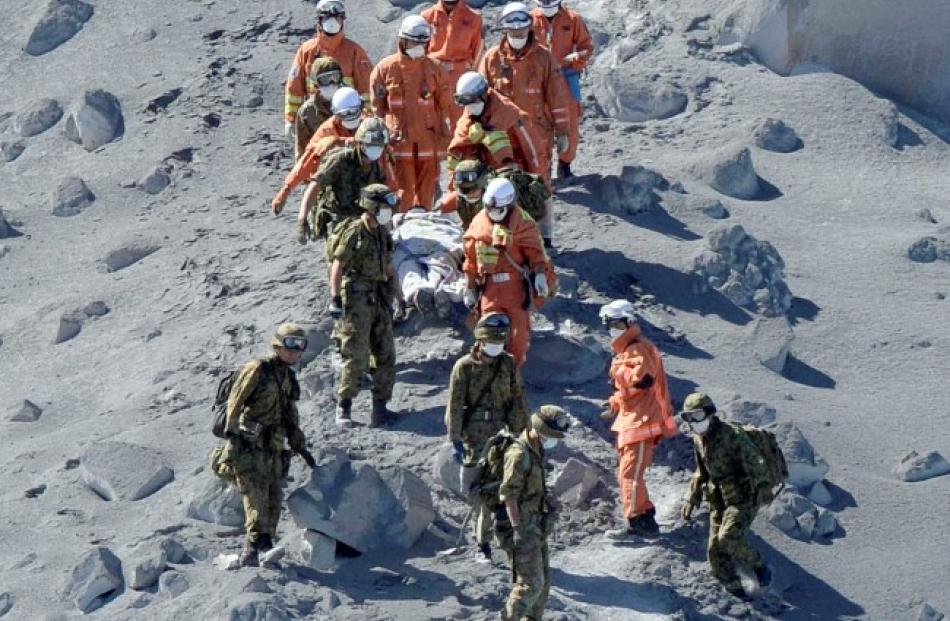 Soldiers and firefighters carry an injured person near a crater of Mt. Ontake yesterday after the...