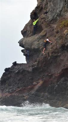 St Clair surf life-saver Rhys McAlevey (top) reaches out to dog Molly up a cliff at Smaills Beach...
