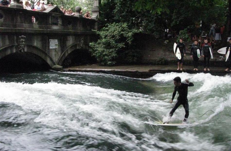 Surfers test their skills on Eisbach (Ice Creek) as it emerges from beneath Himmelreich bridge....