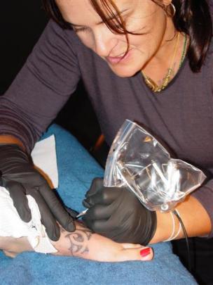 Ta moko artist Julie Paama-Pengelly creates a traditional Maori tattoo on a person's back at a...