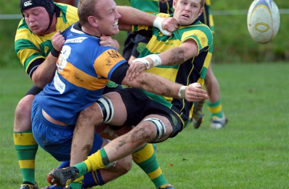 Taieri No 8 Charlie O'Connell slips a pass away despite the tackles of Green Island forwards...