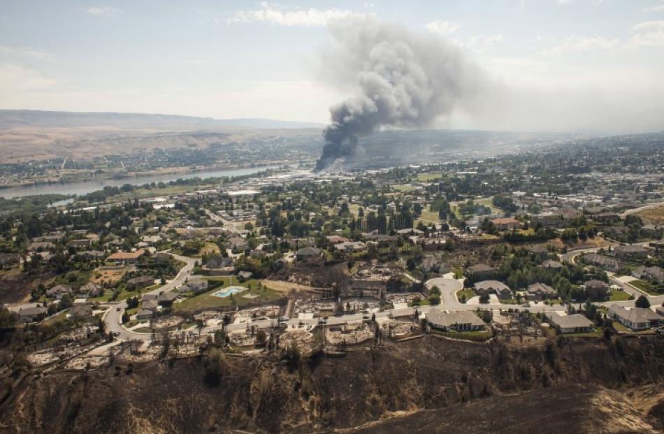 The remains of homes destroyed by the fire are visible in the foreground, as commercial buildings...