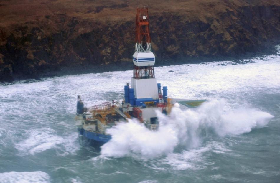 Waves crash over the conical drilling unit Kulluk where it sits aground on the southeast side of...