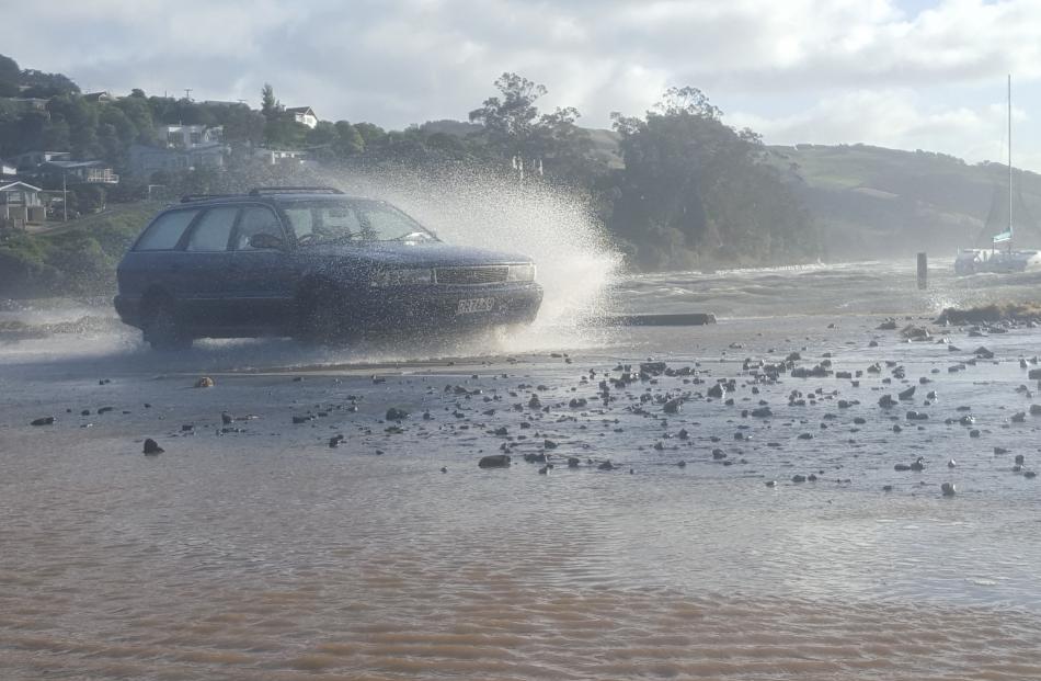 Waves crash over the road at Macandrew Bay. Photo by David Loughrey