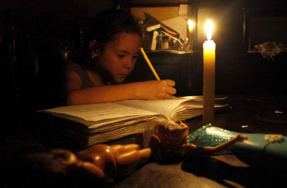 A girl does her homework by candlelight at his home during a power cut in San Cristobal, in the...