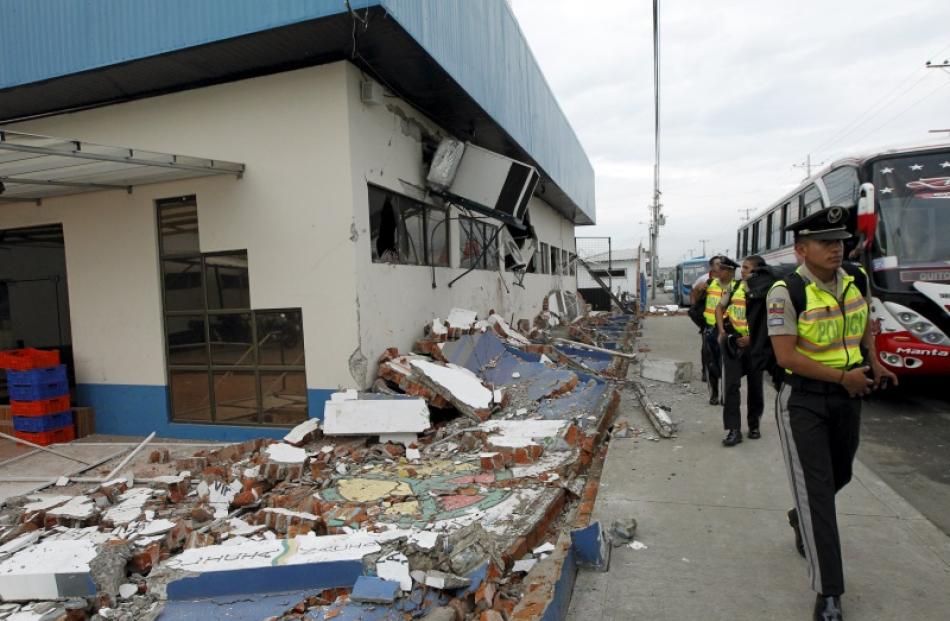 Police officers walk next to debris after an earthquake struck off Ecuador's Pacific coast, at...