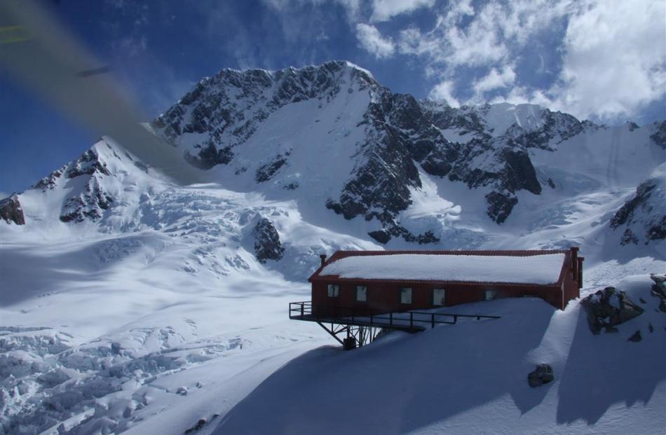 A view from a helicopter of Plateau Hut with Aoraki/Mt Cook behind. A helicopter landing at ‘...