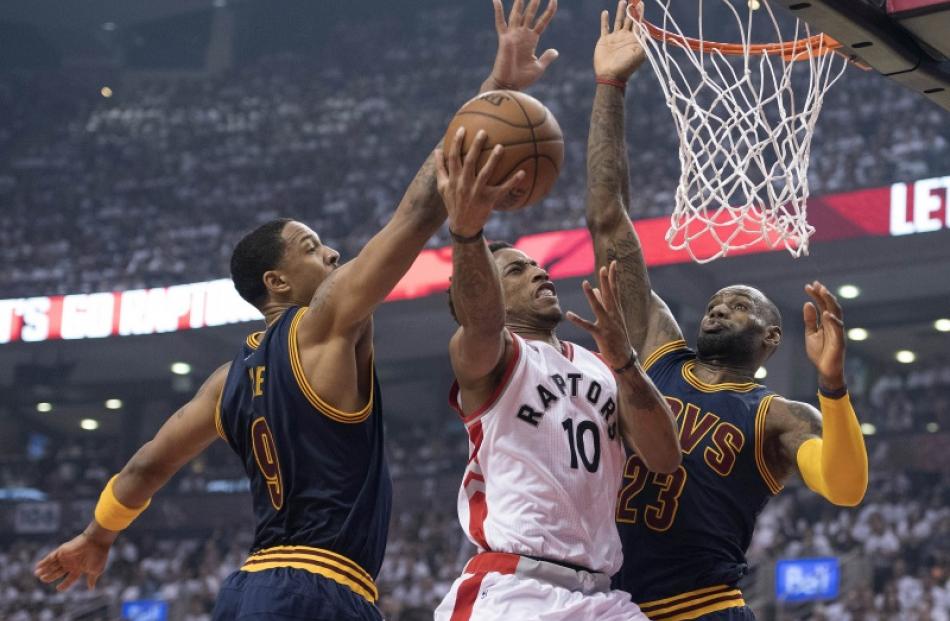 Raptors guard DeMar DeRozan takes the ball to the hoop as Cavs defenders LeBron James and...