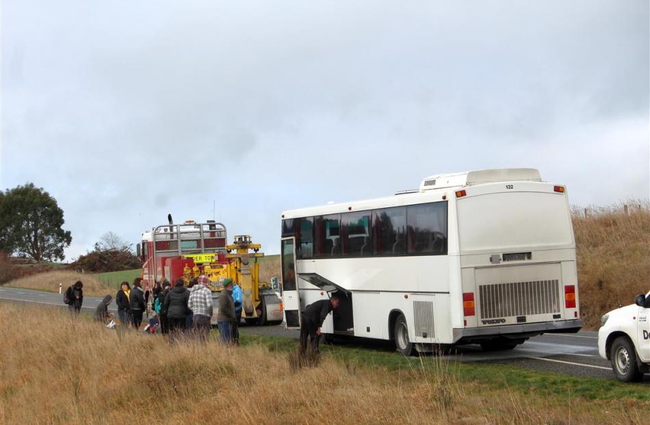 A truck lines up to tow a bus stopped near Clinton after an engine fire, as passengers wait for a...