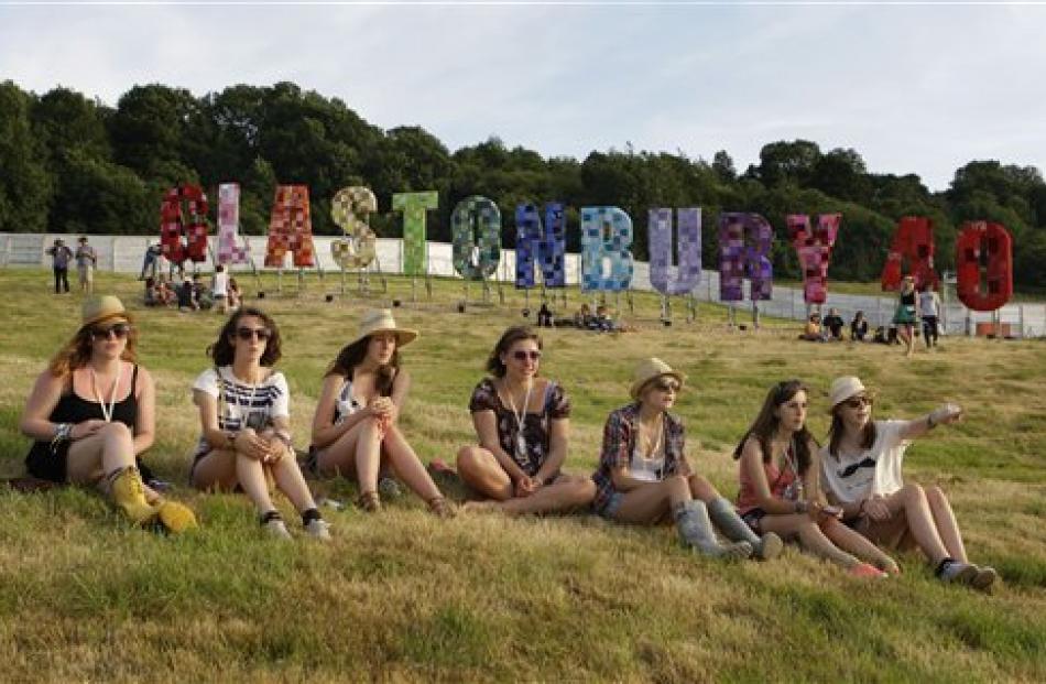 Glastonbury festival goers sit under a large sign on one of the hills.