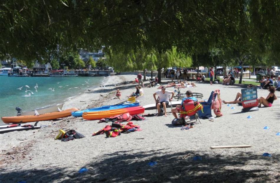 Tourists lounge in 18degC sunshine on the beach of Queenstown Bay yesterday.  Sun and rain is ...