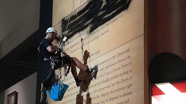A protester abseils inside Te Papa and defaces the Treaty of Waitangi Exhibition. Photo via NZ...